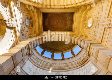 Upward view of ornate stone architecture in Marseille, France, featuring a ceiling panel with a radiating sun face, carved reliefs, circular openings Stock Photo