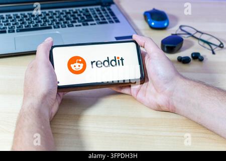 Hand holding a smartphone with the reddit app logo. Stock Photo