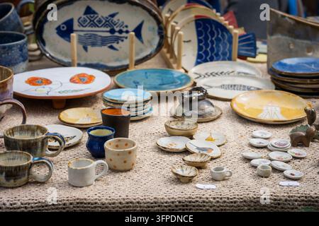 Handcrafted ceramic tableware displayed at an outdoor flea market, featuring blue and white fish plates, colourful pottery, handmade cups. Stock Photo