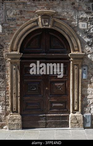 A richly decorated dark wooden door with stone arched frame adorns the facade of a historic house, Gubbio, Umbria, Italy Stock Photo