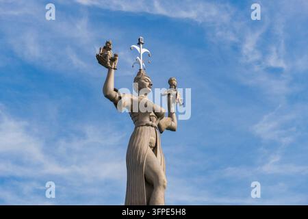 Taken from the side, a monumental statue of a woman holding two small figures in front of the sky, Imperia statue in the port of Constance on Lake Con Stock Photo