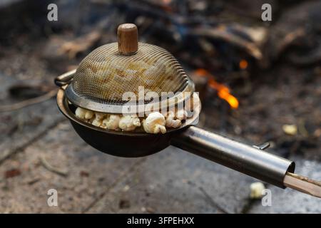 Popcorn made in a popcorn maker, fresh from the campfire burning in the background. Stock Photo