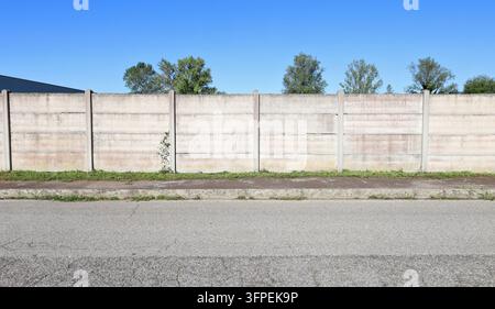 Concrete precast compound wall at the road side. Sidewalk and road in front, trees and sky on behind. Background for copy space Stock Photo