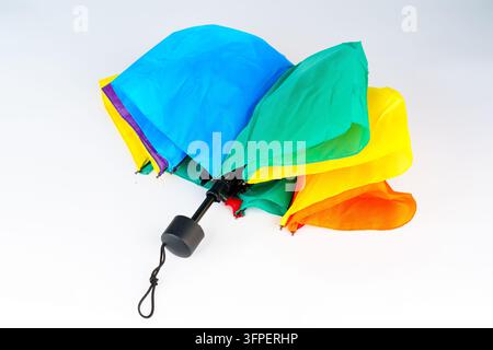 Colorful folding umbrella with rainbow colored panels resting on a plain white background. Compact telescopic design showcases vibrant shades of blue, Stock Photo