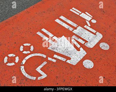A close-up view of a white painted pictogram on a red painted asphalt surface, showing a stylized figure pushing a shopping cart. The paint is heavily Stock Photo