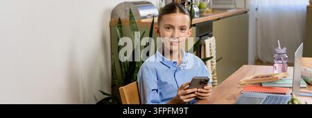 A girl engaged in her homework using a smartphone in a comfortable study area, banner Stock Photo