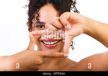 A young Hispanic woman demonstrates skin health by framing her face with her hands. She is smiling, engaging viewers with her beauty. The scene takes Stock Photo