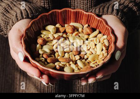 Woman holding brown bowl of assorted mixed nuts in hands. Healthy snack background for peanuts almonds cashews nutrition protein and natural food. Stock Photo