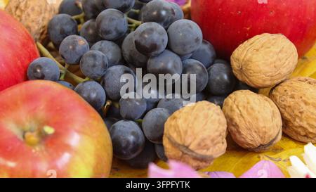 Red apples, dark grapes, and walnuts are displayed on a surface surrounded by colorful flowers. This arrangement adds a touch of natural beauty to the Stock Photo
