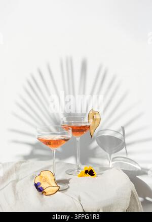 Two rose wine glasses with summer cocktails and dried fruit appetizers. Tropical light background with palm shadow. Stock Photo