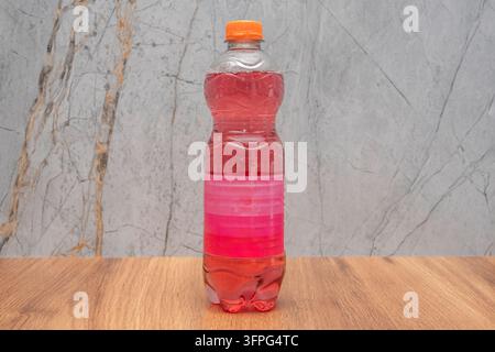 Plastic bottle with pink soda and orange cap on a wooden table with a marble background. Stock Photo