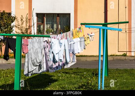 Assorted clothing items and towels hang to dry on outdoor clotheslines fastened with wooden and plastic pegs outside a residential building. Bright af Stock Photo
