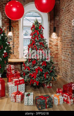 Christmas tree decorated with red bows and gifts in a festive brick interior Stock Photo