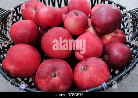 Close up top view of a black wicker basket filled with ripe red apples. Fresh sweet organic fruit crop harvested in an autumn garden, healthy natural Stock Photo