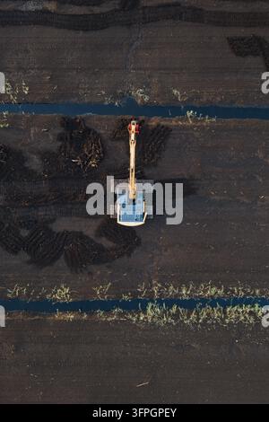Vertical aerial top down view of yellow tracked excavator working on dark peat extraction bog field with drainage canals in Omma Estonia. Stock Photo