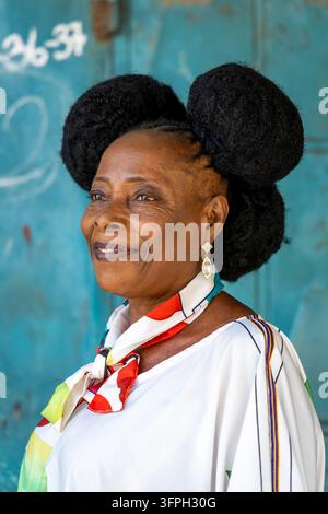 An elderly woman with a distinctive twin bun hairstyle smiles in profile view, Central Region, Elmina, Ghana Stock Photo