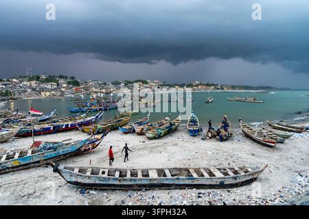 Dark storm clouds gather over a busy fishing harbor filled with wooden boats, Central Region, Cape Coast, Ghana Stock Photo