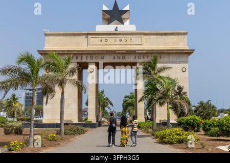 A group of young visitors walk along a palm lined path toward the Black Star Gate monument, Greater Accra Region, Accra, Ghana Stock Photo