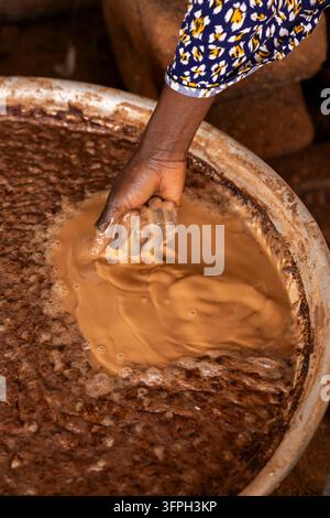 Close up of a hand kneading shea butter paste in a large metal basin, Northern Region, Tamale, Ghana Stock Photo