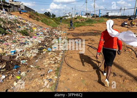 Woman in red jacket and white headscarf walking beside a rubbish slope and railway in Kibera area, Nairobi County, Nairobi, Kenya Stock Photo