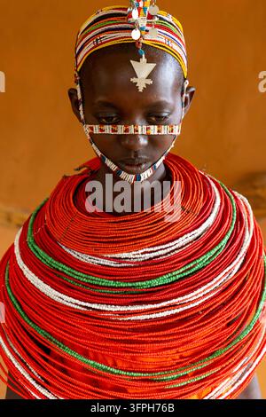 Close-up of a Samburu tribe woman looking down wearing a beaded face band a silver forehead pendant and a huge layered red and green bead collar, Samb Stock Photo