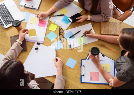 Team collaboration and brainstorming, diverse colleagues working together on business strategy with sticky notes and documents on a wooden office desk Stock Photo