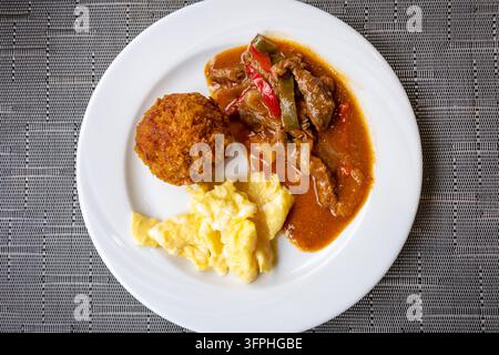 Traditional Ecuadorian bolon de verde served with savory beef stew and fluffy scrambled eggs Stock Photo