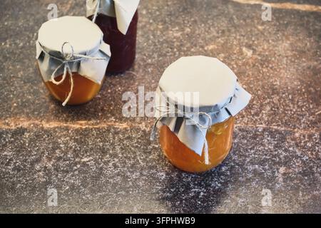 Three jars of fruit jam sealed with paper and string on dark countertop Stock Photo