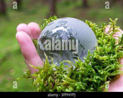 A glass globe containing fresh green moss held carefully in a human hand, symbolizing environmental protection, nature conservation, and responsibility for our planet. The delicate ecosystem represents sustainability, biodiversity, climate awareness, ecolo Stock Photo