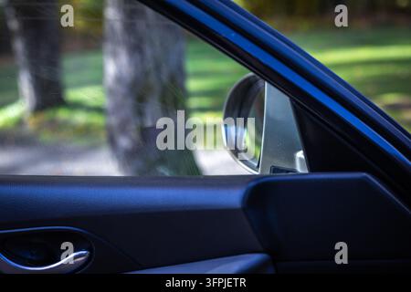 View from inside car door frame looking at side mirror and autumn park background Stock Photo