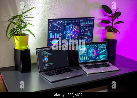 Stylish home office desk featuring two laptops, a large monitor with data visualizations, ambient colored lighting, and potted plants. Stock Photo