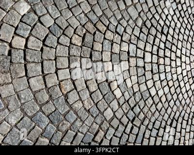 Detailed background texture of a historic European street paved with grey granite cobblestones arranged in an artistic curved fan pattern. Stock Photo