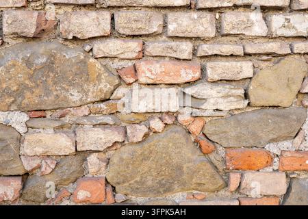 A close-up view of a rough rustic stone wall made of mixed masonry blocks. Stock Photo