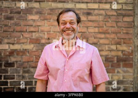 A smiling middle aged man stands in front of a brick wall. Stock Photo