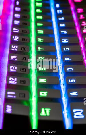View along gaming keyboard with vibrant rainbow LED back lighting, combining technology and entertainment. Keys illuminated in green, blue and purple. Stock Photo