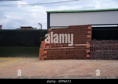 BOGOTA, COLOMBIA - NOVEMBER 1 2025: A large pile of red hollow ceramic bricks stacked outside a fenced warehouse in an urban construction supply yard Stock Photo
