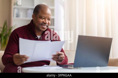 Senior black man reviewing printed documents beside laptop at home Stock Photo