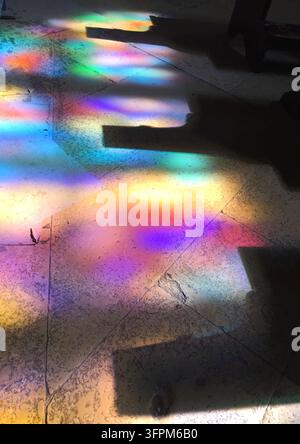 Abstract play of colorful light reflections on a stone floor, created by sunlight streaming through stained glass windows inside a historic church. Vi Stock Photo