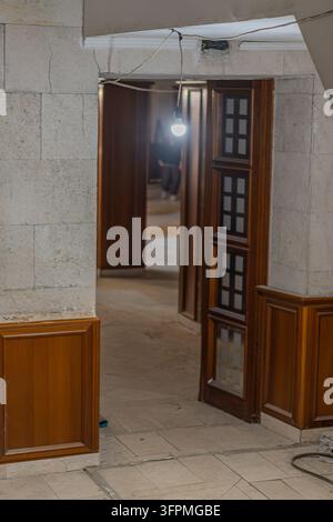 Kitchen doorway framed by unfinished rustic cabinetry under renovation, warm medium-toned wood, light stone tiles, dimly lit room beyond, single hangi Stock Photo