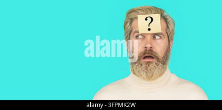 Surprised bearded man with question mark on blue background. Man with question mark on forehead looking up. Paper notes with question marks. Copy Stock Photo