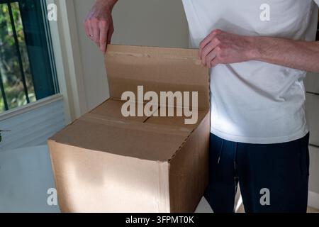 Man opening large cardboard shipping box indoors, close-up of hands unpacking parcel Stock Photo