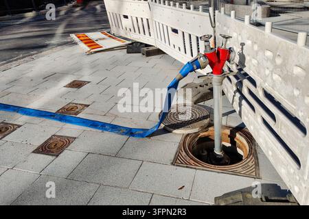 Espoo, Finland - October 2nd, 2026: A temporary water supply setup with a red fire hydrant and a blue hose installed near an open manhole on a paved s Stock Photo