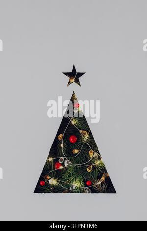 Triangular Christmas tree cut out in gray cardboard with lighted garland and Christmas tree branches. Stock Photo