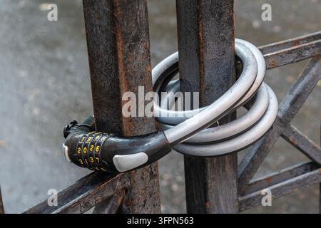A silver and black coded lock is wrapped around a metal gate. Bicycle lock on the metal gate. Stock Photo