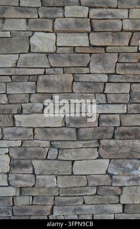 Varied rectangular stone bricks with scratches, surface cracks and a fossil-like indentation, forming a vertically composed masonry wall Stock Photo