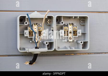 Double outdoor socket installation on gray wooden wall shows open casing and exposed wires, clearly demonstrating step-by-step connection process. Stock Photo