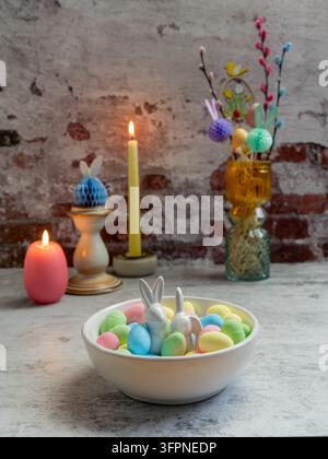 Easter still life featuring pastel artificial eggs arranged in a bowl with candles and colorful spring branches in a decorative vase Stock Photo