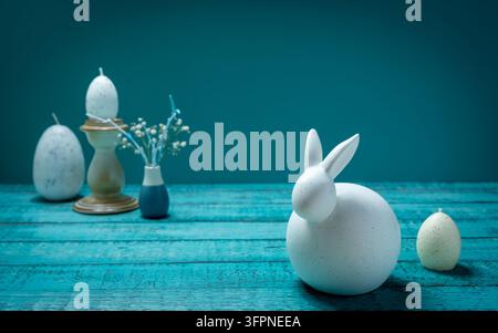 Minimal Easter still life featuring a white bunny figurine decorative egg and candle arranged with a small spring flower arrangement Stock Photo