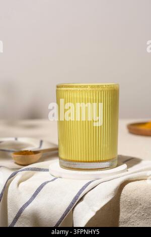 Sunny turmeric latte in ribbed glass stands on striped linen in soft daylight, radiating calm comfort and warm wellness mood Stock Photo
