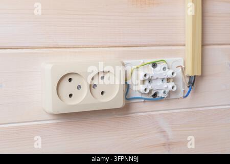 Double electrical socket installation in progress, exposed colored wires ready for connection on modern wooden wall interior. Stock Photo